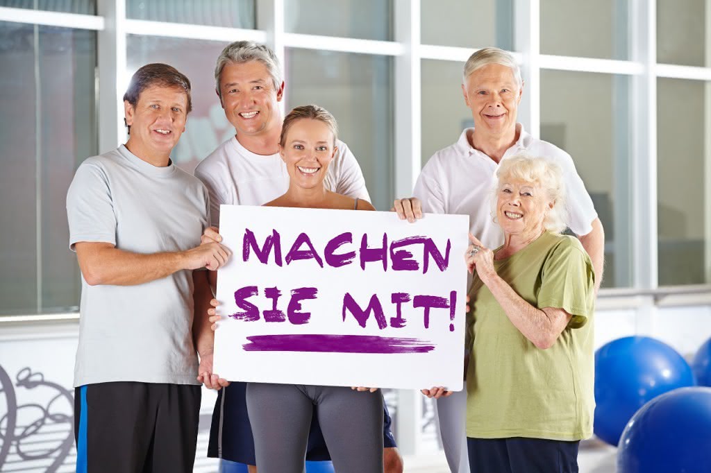 Gruppe Senioren hält "Machen sie mit" Schild im Fitnesscenter