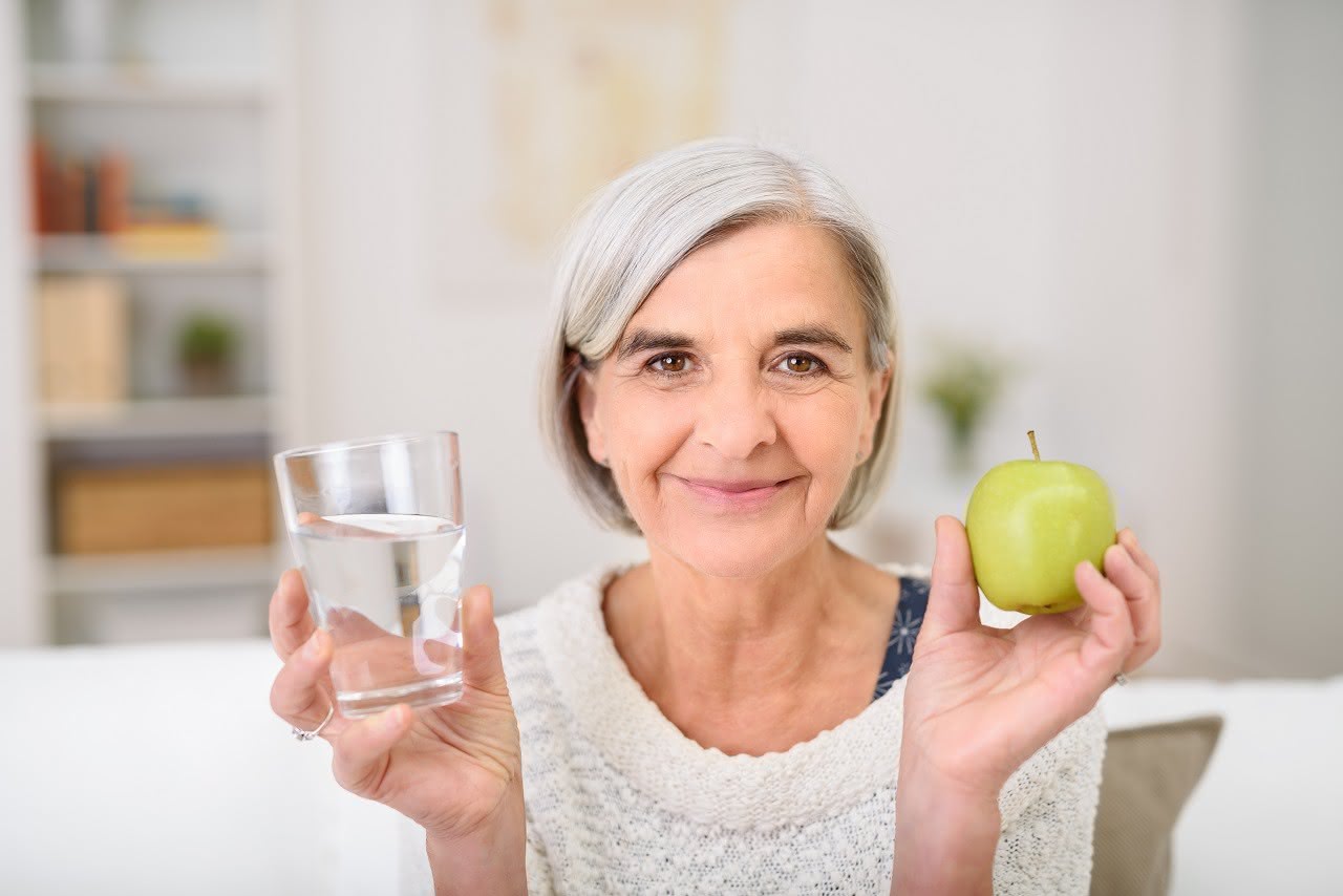 Seniorin hält Wasserglas und Apfel in den Händen