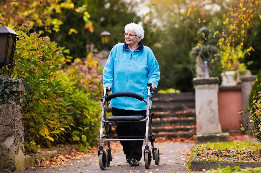 Seniorin spaziert mit Rollator im Park