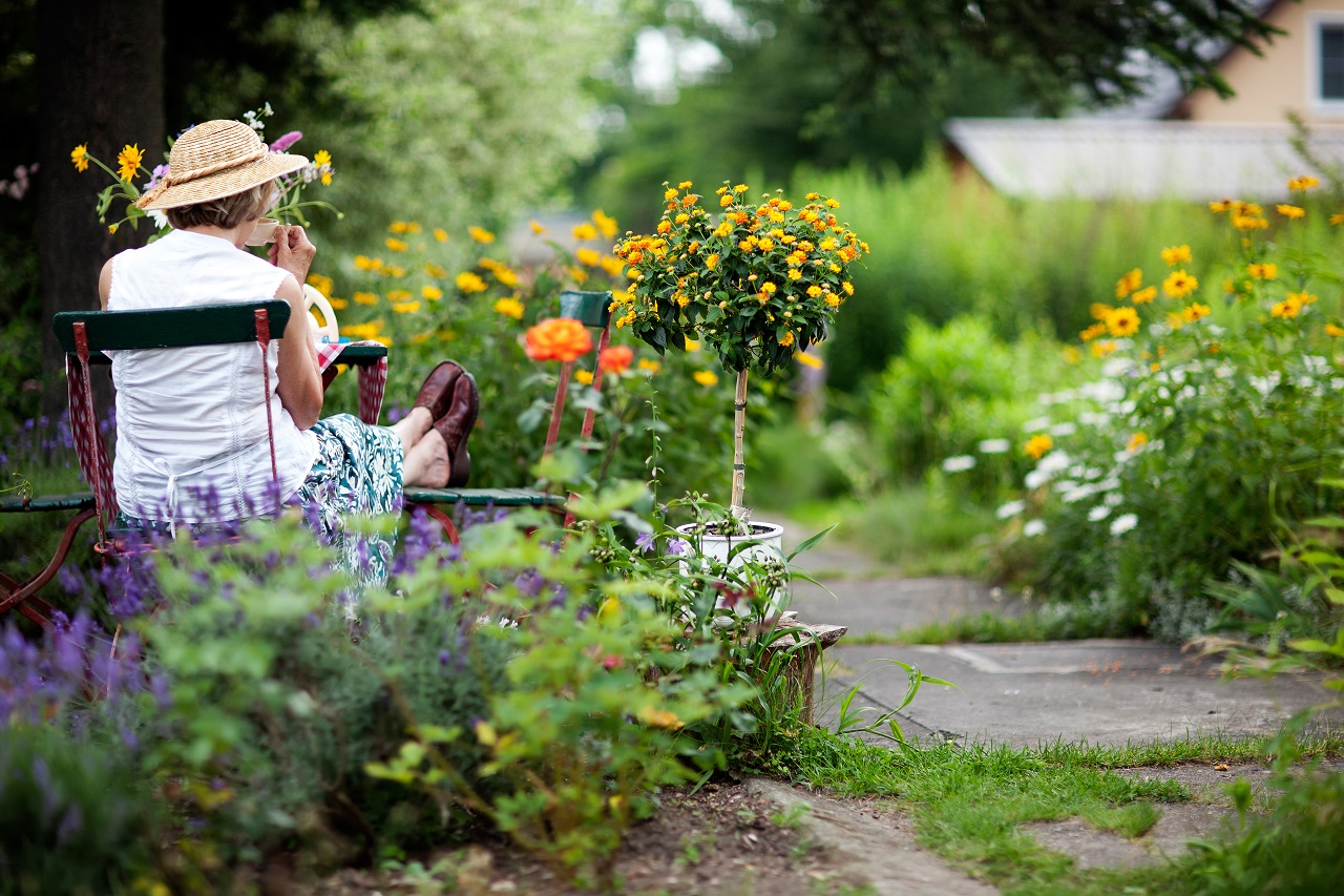 Seniorin entspannt sich auf einem Stuhl im Garten bei einem Getränk